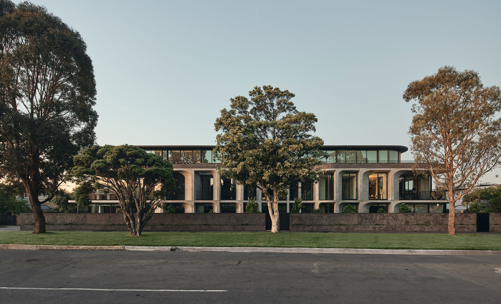 Landscape image of minimalist, modern architectural building with lush green foliage, concrete facade and curved glass windows.