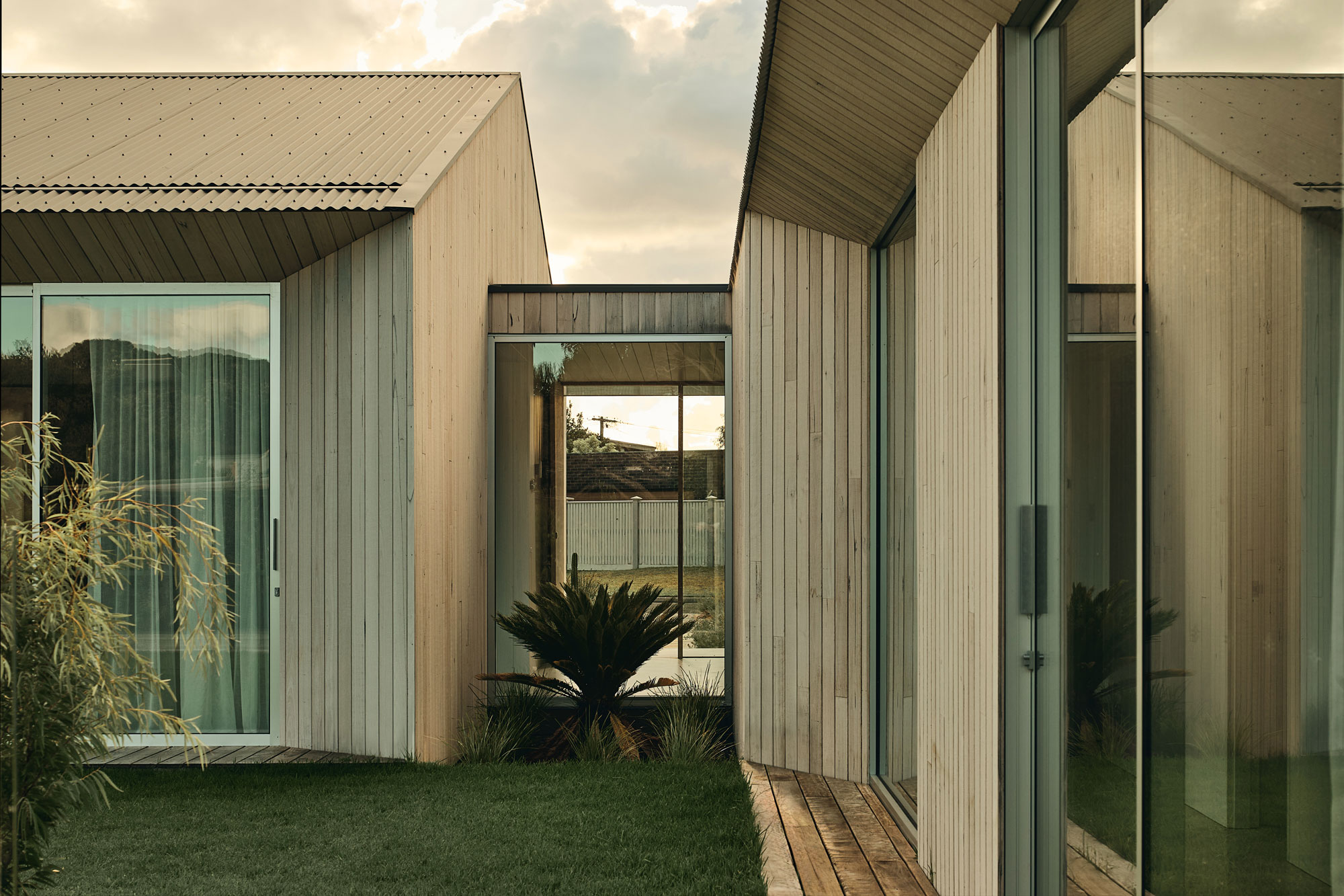 Soft morning light shows modern timber home with large scale windows and lush landscaping.