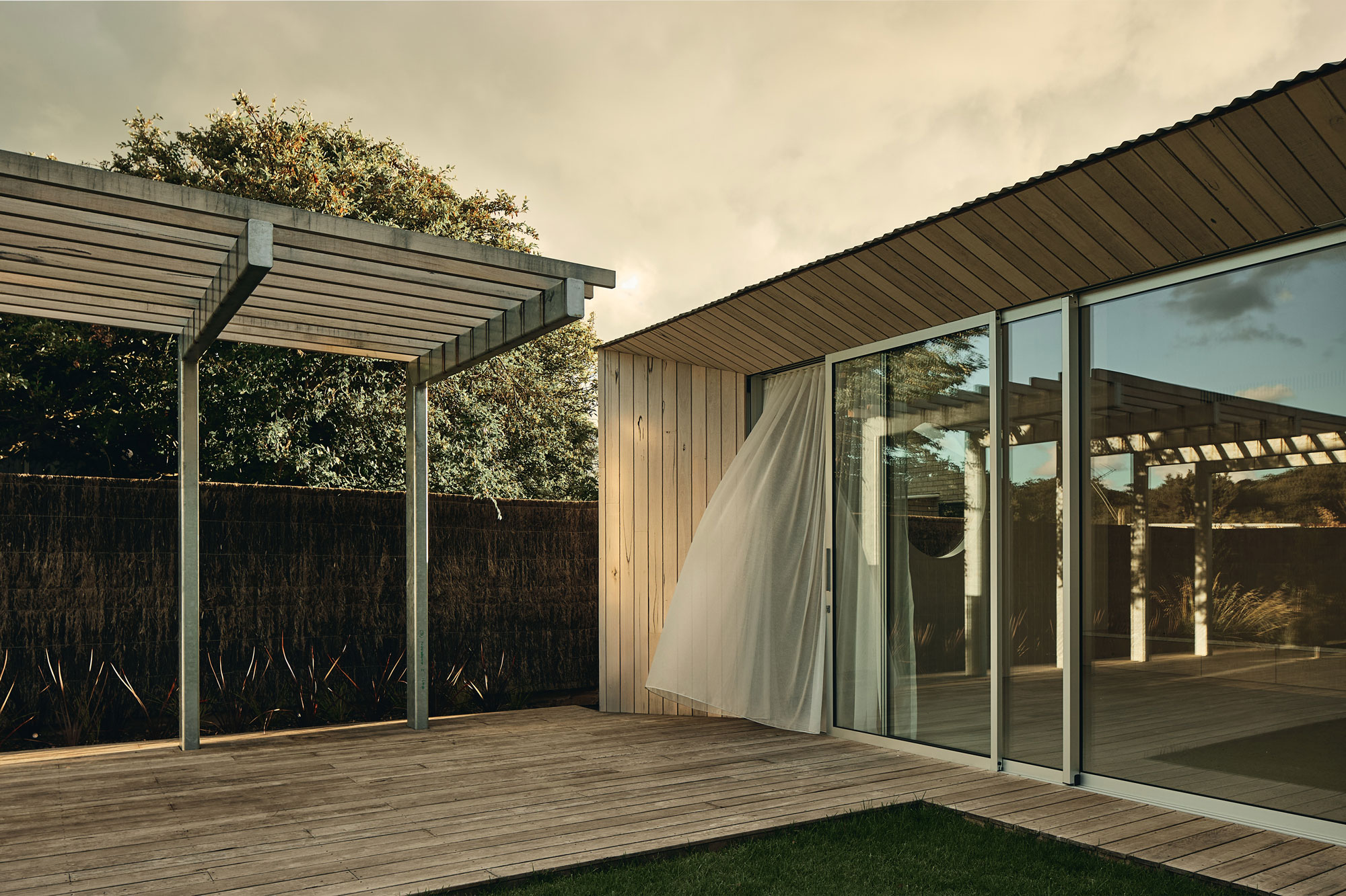 Soft morning light shows modern timber home with large scale windows and large decking area.