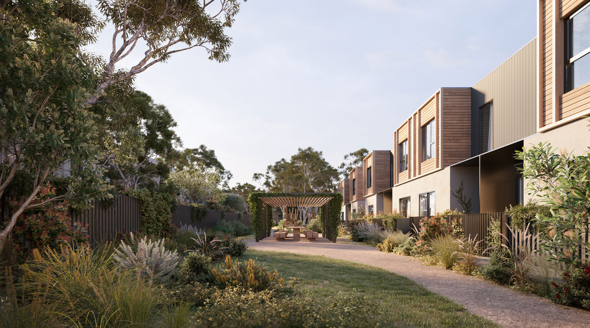 Lush landscaping surrounds a communal outdoor seating area positioned in front of timber clad townhouses.