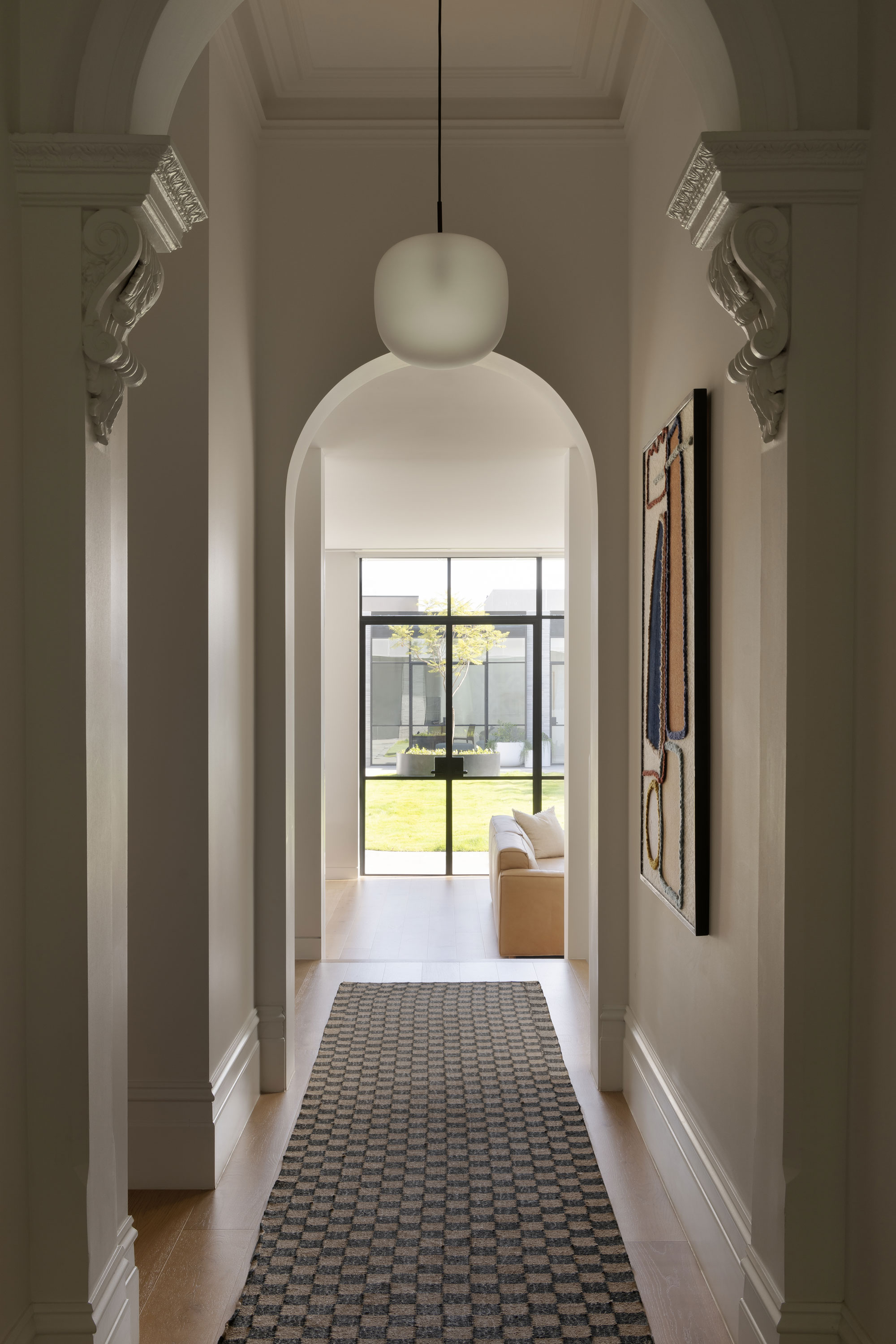 A long hallway with heritage detailing lined with a decorative rug that leads to large-double glass doors that open up to a lush green yard.