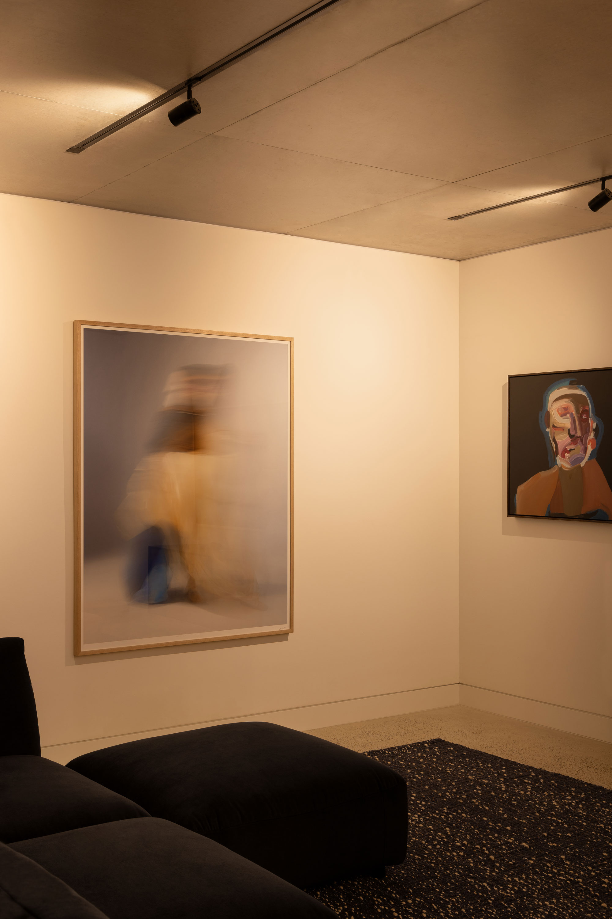 Contemporary room with two abstract artworks hanging on adjacent walls, polished concrete ceiling with industrial style light strips.