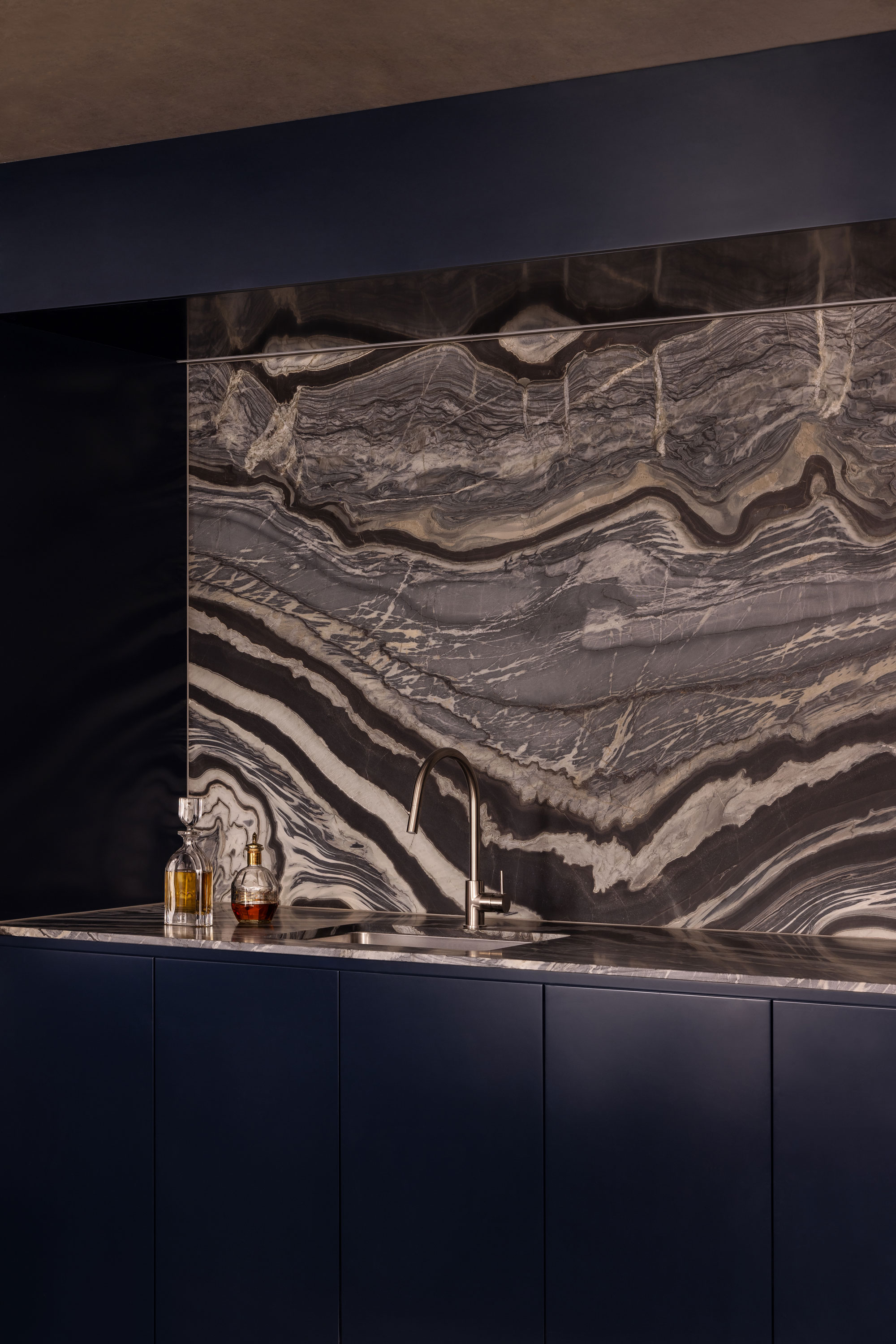 Contemporary navy blue bar with detailed marble splash back, chrome tap and 2 glass liquor bottles.