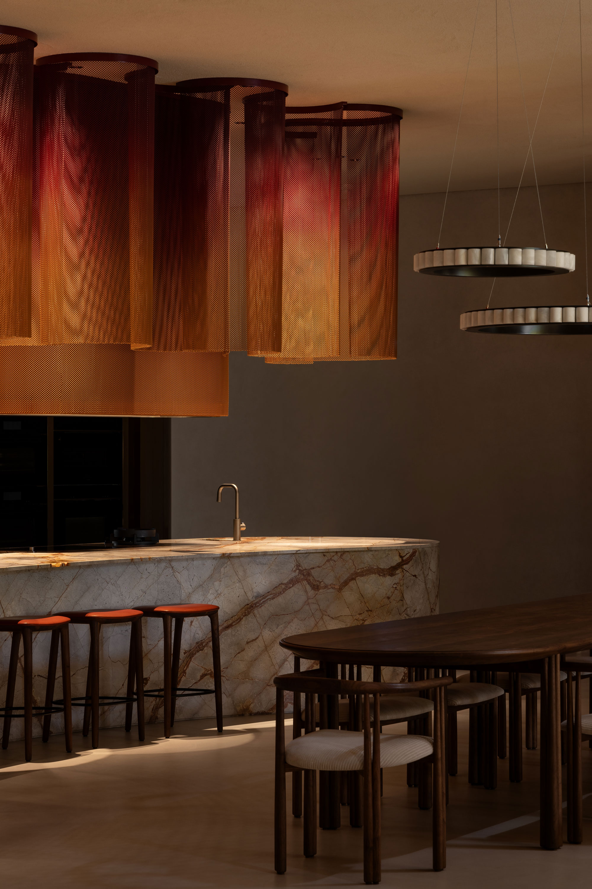 Luxurious modern kitchen with sculptural lighting fixtures, large marble island bench set along side a long line dining table with matching seating.