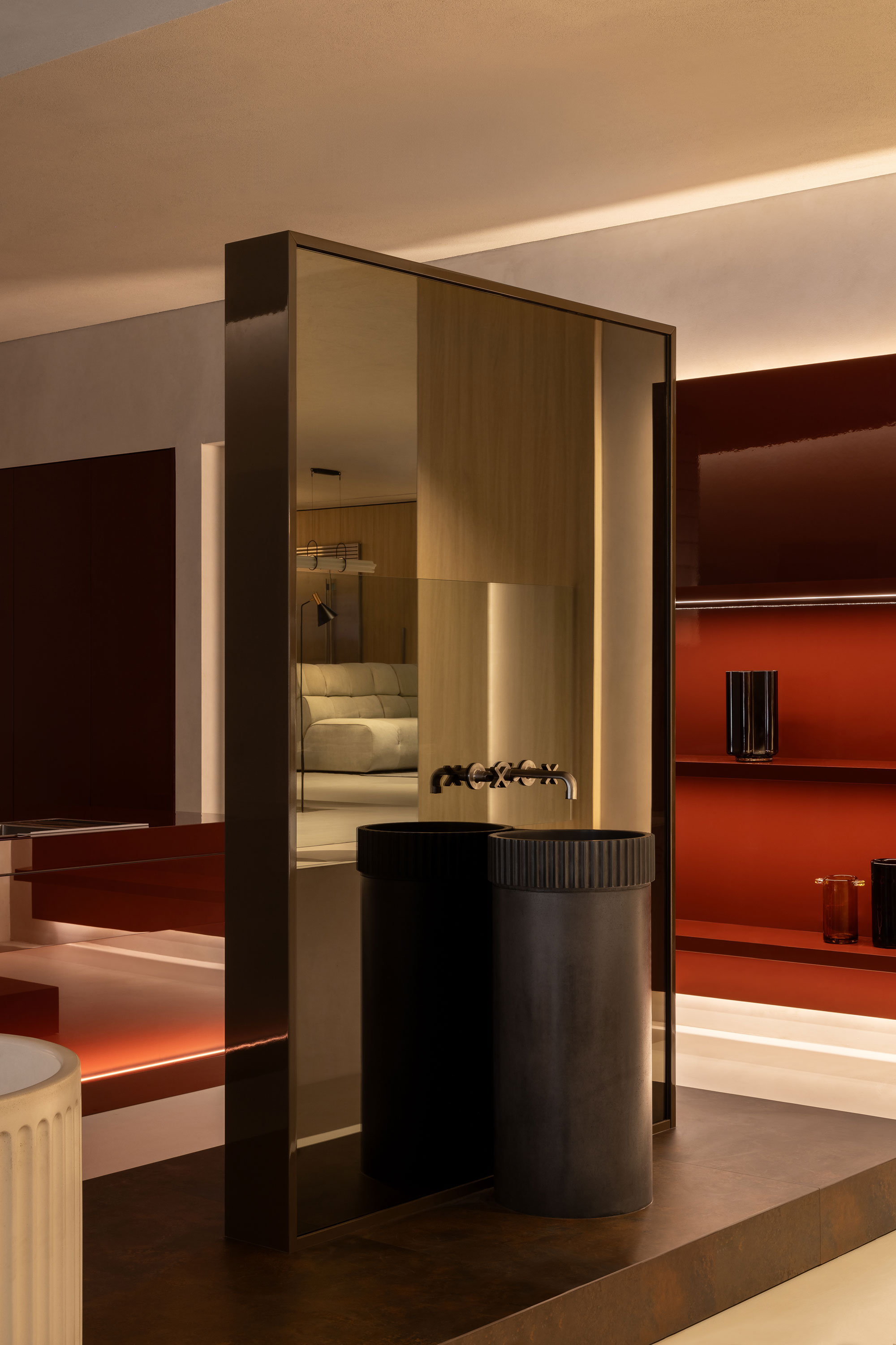 Angled shot shows mirrored wall with round vanity set in front of a wall painted in warm hues with moody lighting.