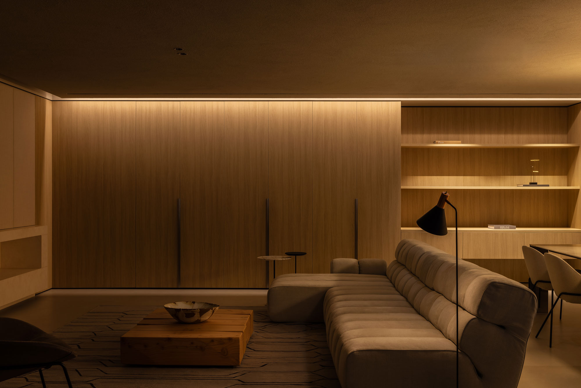 Landscape image of spacious lounge room with a neutral colour palette and warm moody lighting.