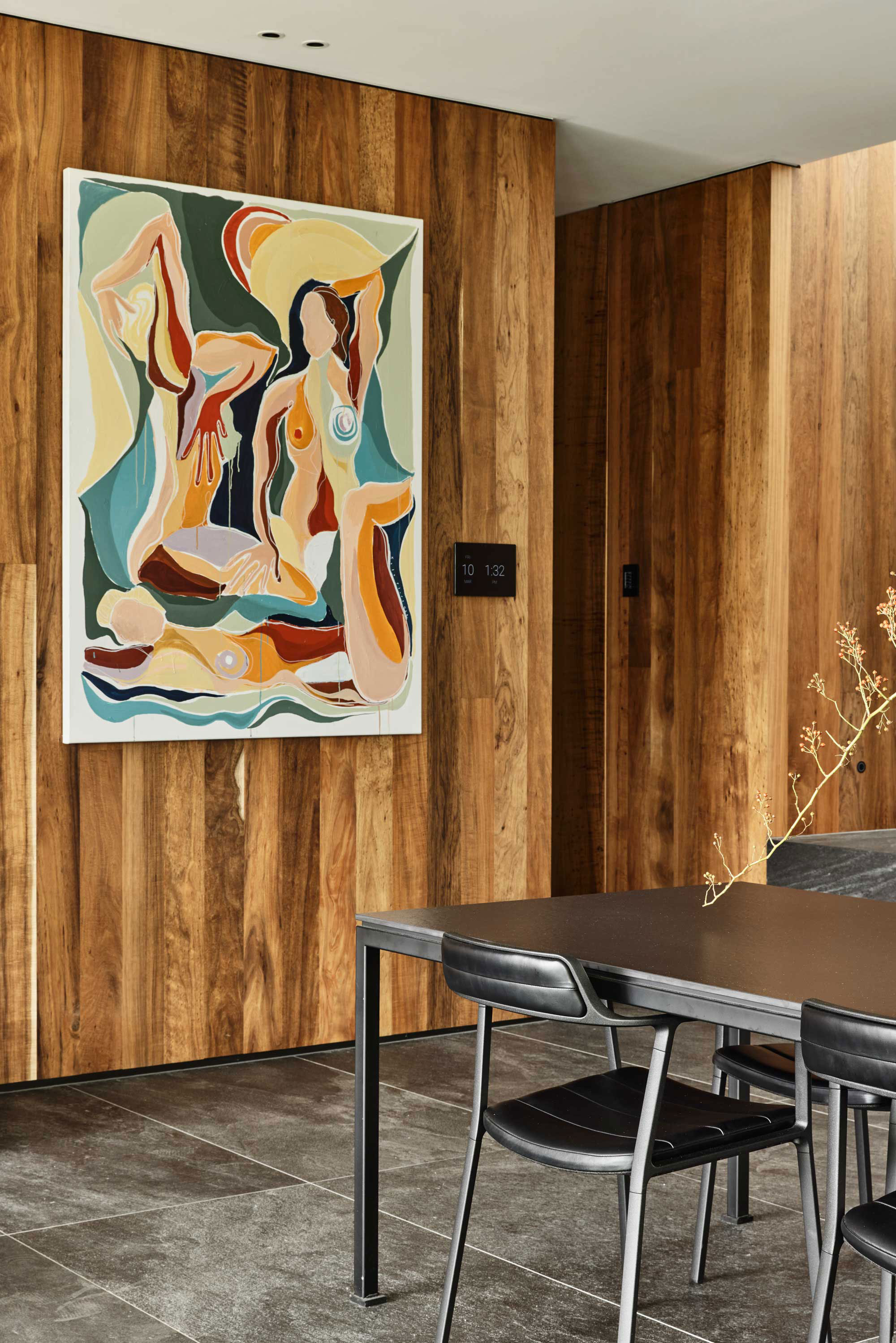 Modern industrial dining space with warm timber panelling, abstract artwork and sleek black furniture.