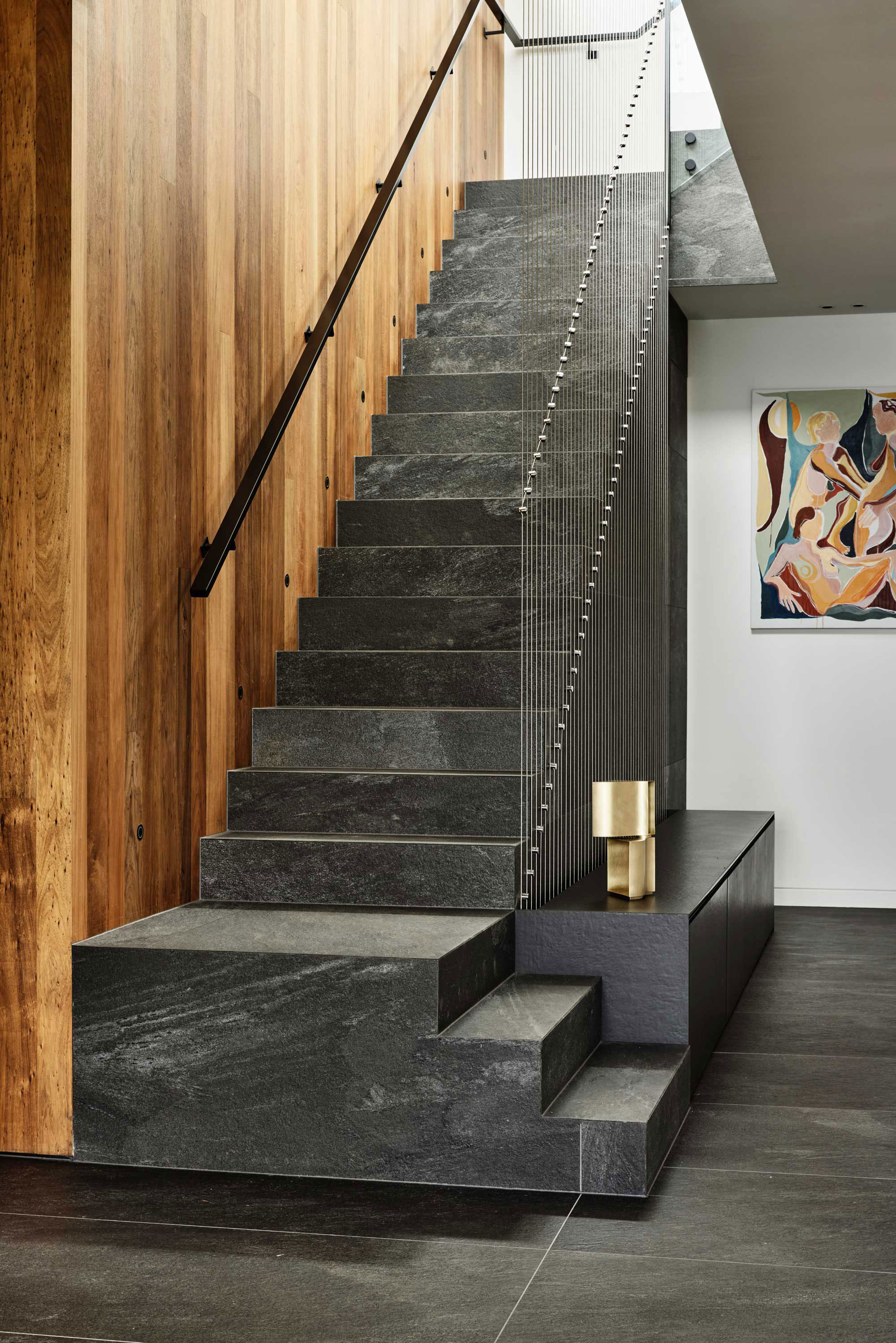 Concrete staircase with warm timber panelled walls, artistic metal balustrade and abstract colourful artwork.