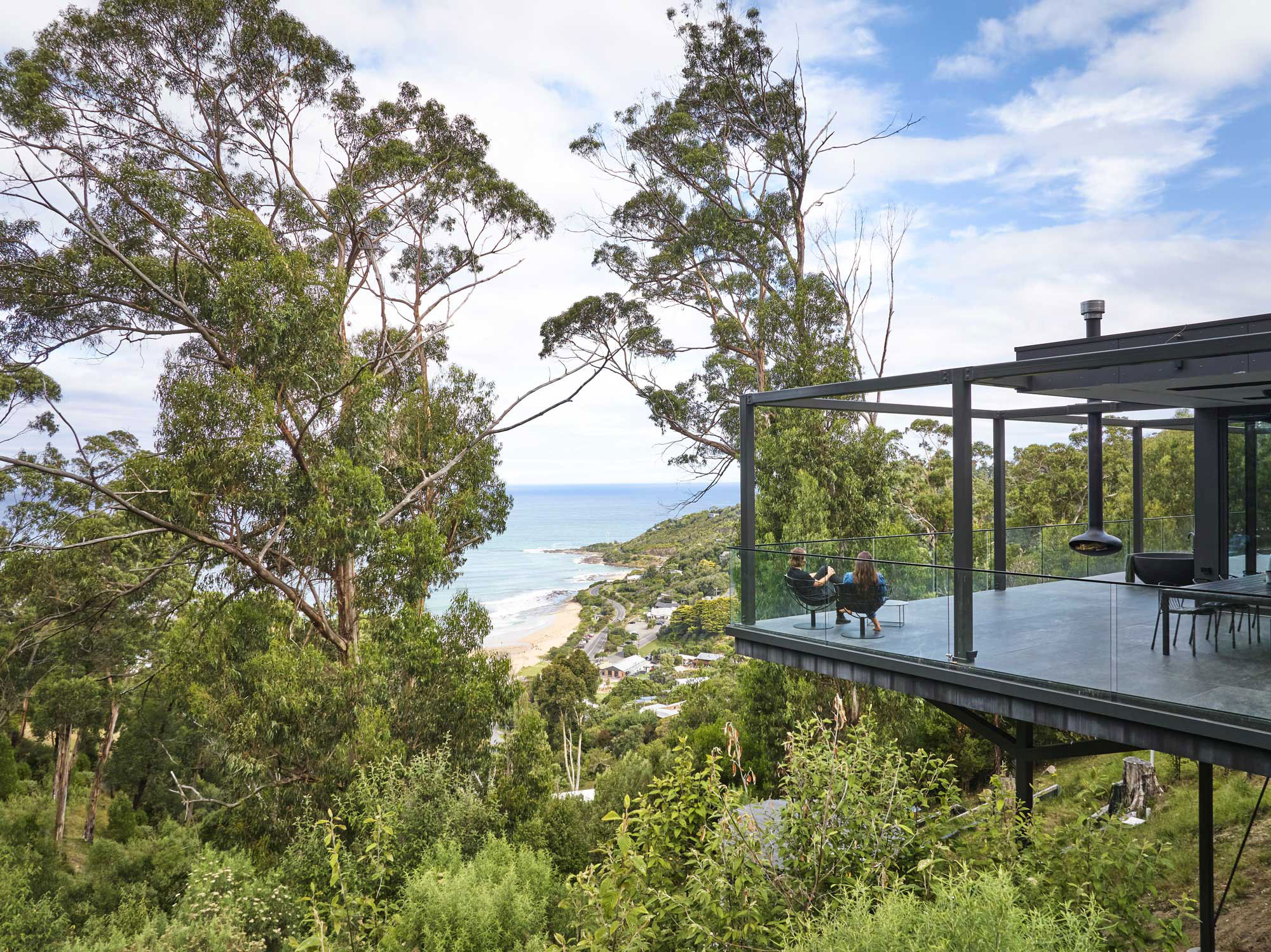 Corner balcony with two people overlooking lush greenery and ocean views.