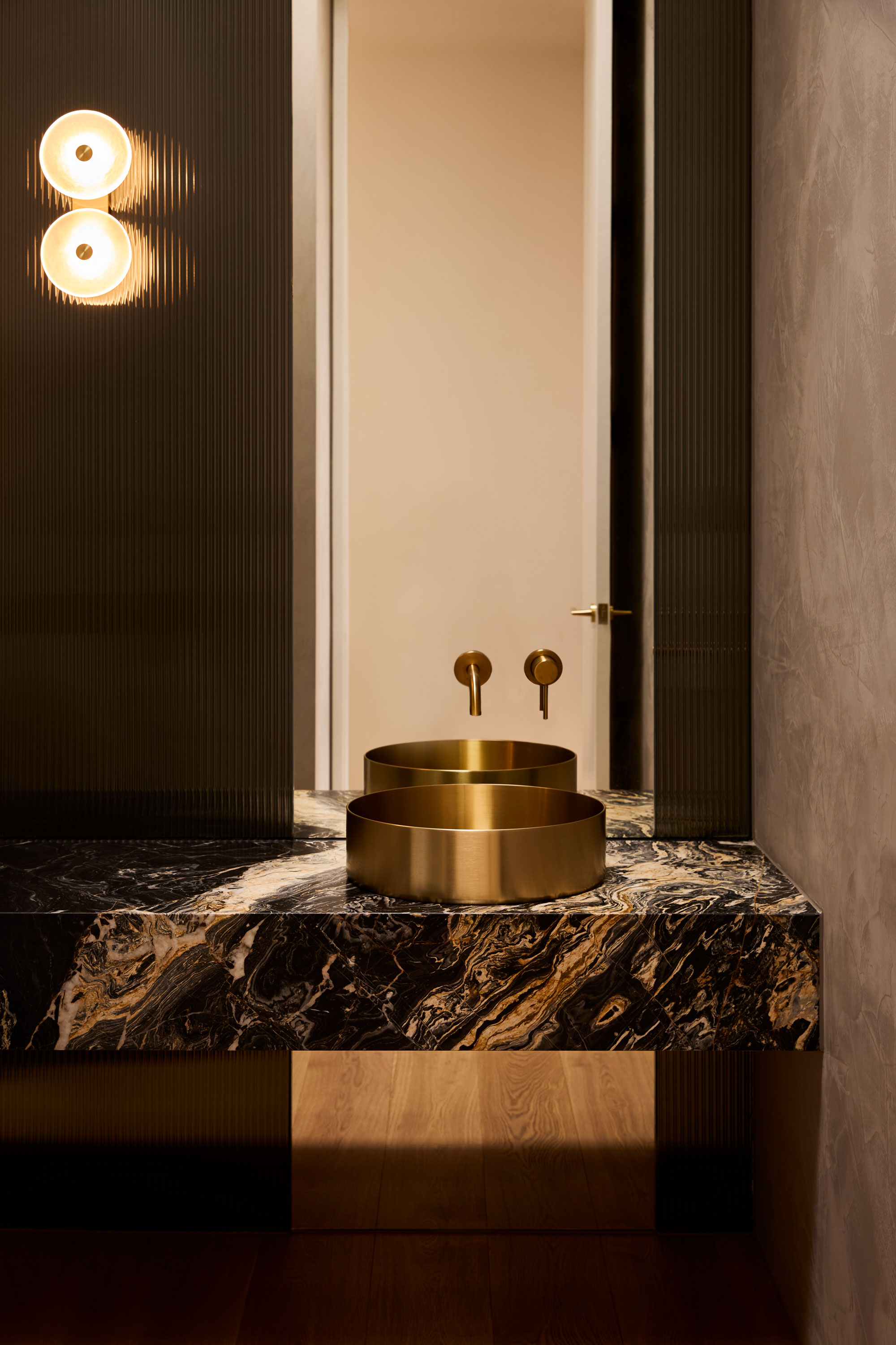 Moody modern powder room with feature marble bench top, brass basin and off-centre wall sconce.